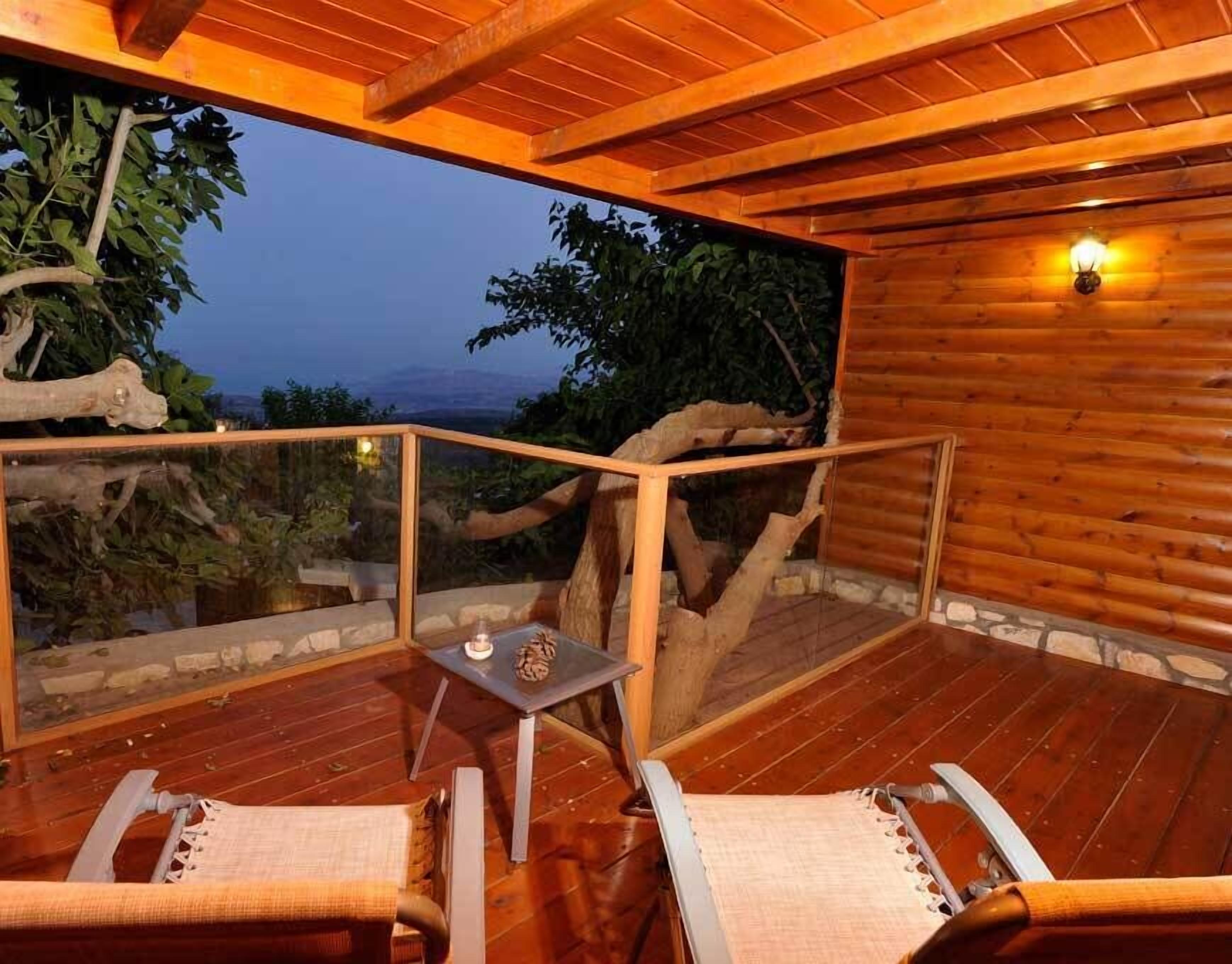 A wooden deck with two lounge chairs and a small table, overlooking a natural landscape.