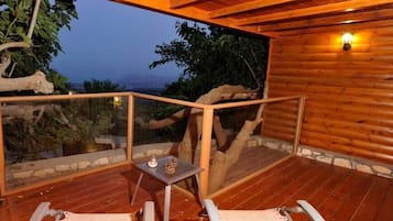 A wooden deck with two lounge chairs and a small table, overlooking a natural landscape.