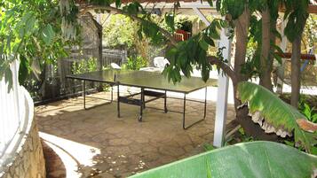 Une table de ping-pong installée dans un espace extérieur, avec un sol en pierre et entourée de verdure.