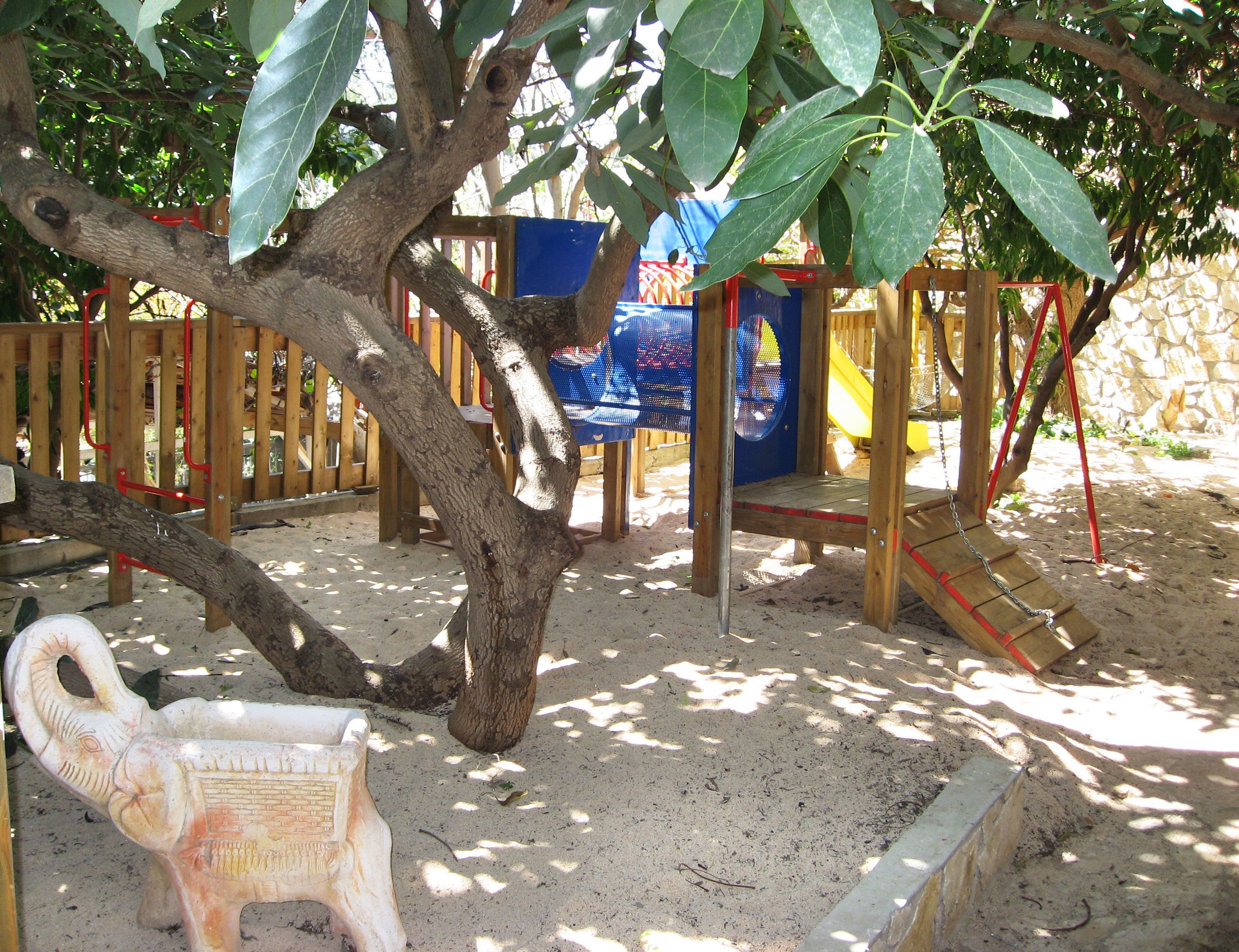 A playground with a slide, climbing structures, and a tree.