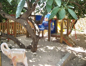 Un parque infantil con un tobogán, estructuras para escalar y un árbol.