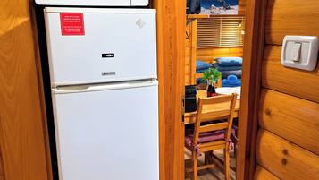 A compact kitchen with a microwave and refrigerator, wooden walls, a dining area with a table and chairs, and a visible light switch.