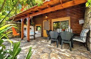Uma cabana de madeira com um alpendre de pedra, banheira de hidromassagem e área de estar externa.