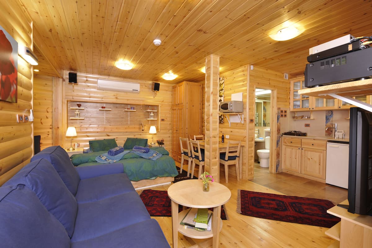 A wooden cabin interior with a sofa, dining table, chairs, a kitchen area, and a bathroom.