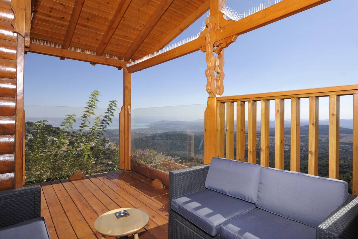 A wooden deck with a sofa and table, overlooking a mountainous landscape.