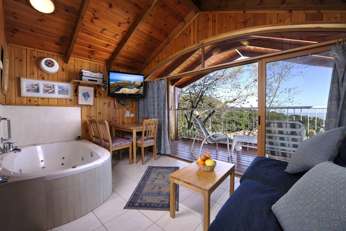 A wooden cabin with a large bathtub, a dining area, and a balcony with a view.