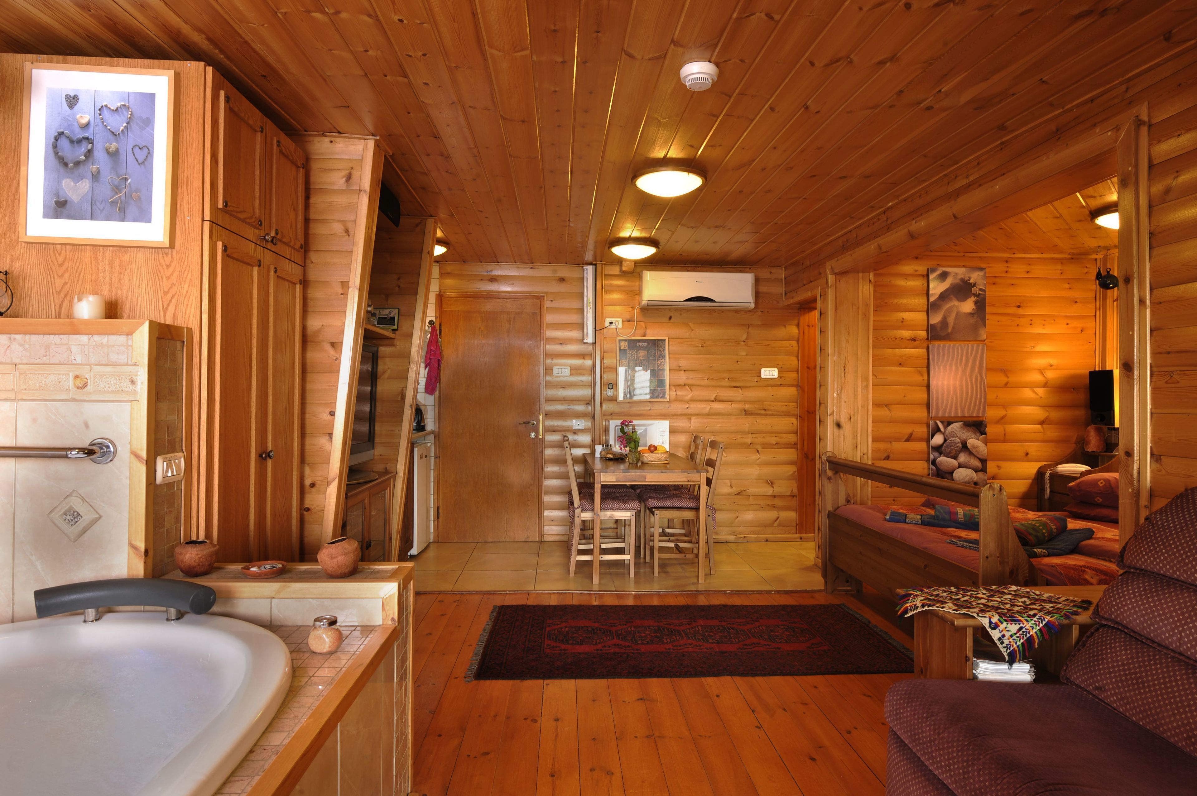 Interior de una cabaña de troncos con una mesa de comedor de madera, un sofá, una bañera y una chimenea.