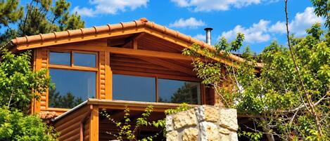 Una cabaña de madera con base de piedra, ventanas amplias y una chimenea.