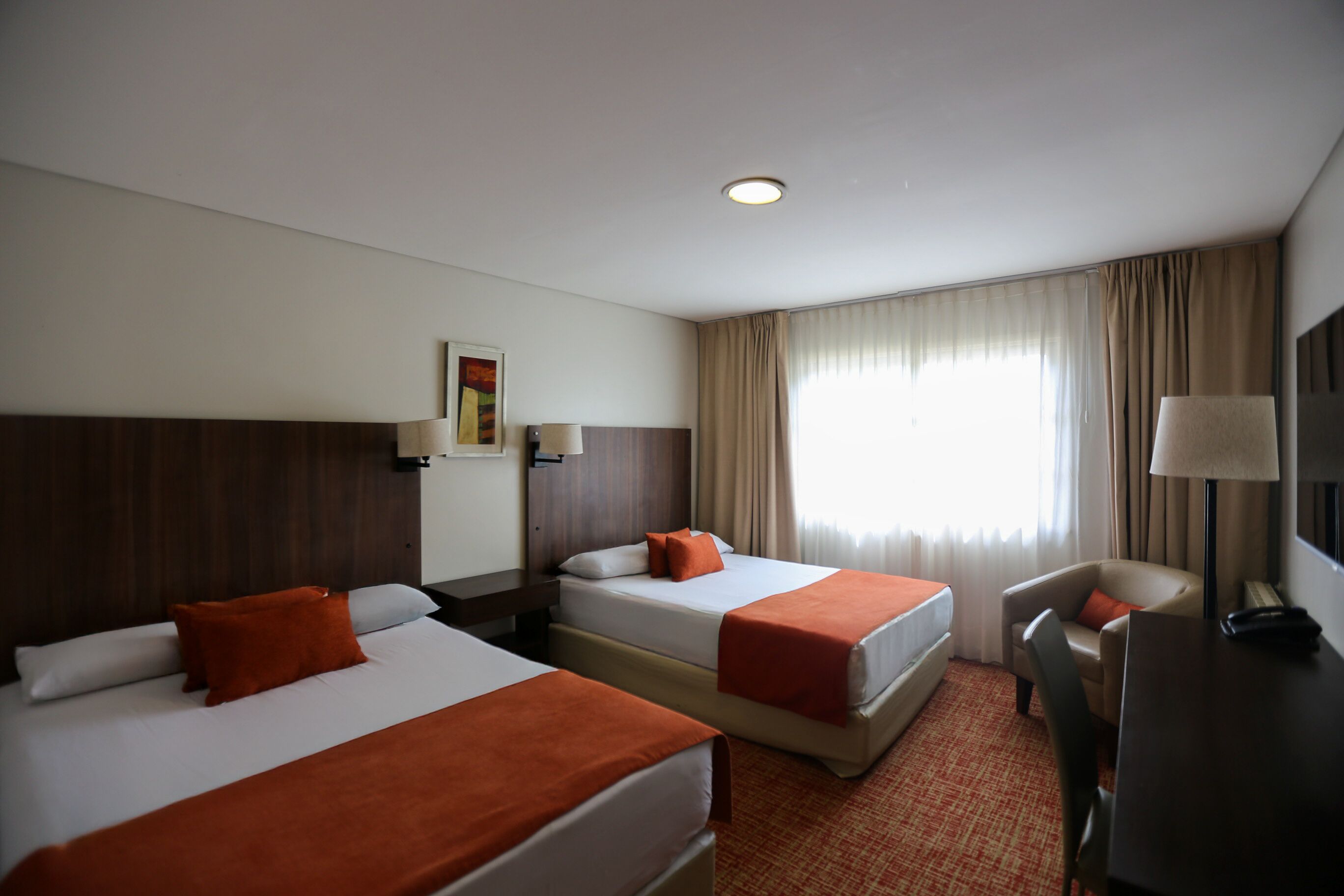 Habitación de hotel con dos camas, un escritorio, una silla y un televisor.