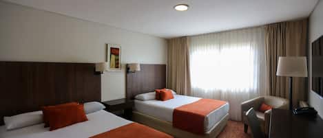 A hotel room with two beds, a desk, a chair, and a TV.