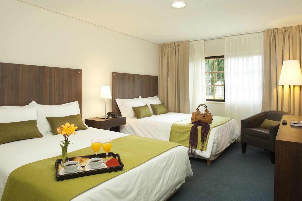 Une chambre d’hôtel avec deux lits, un bureau, une chaise, une télévision et une fenêtre avec des rideaux.