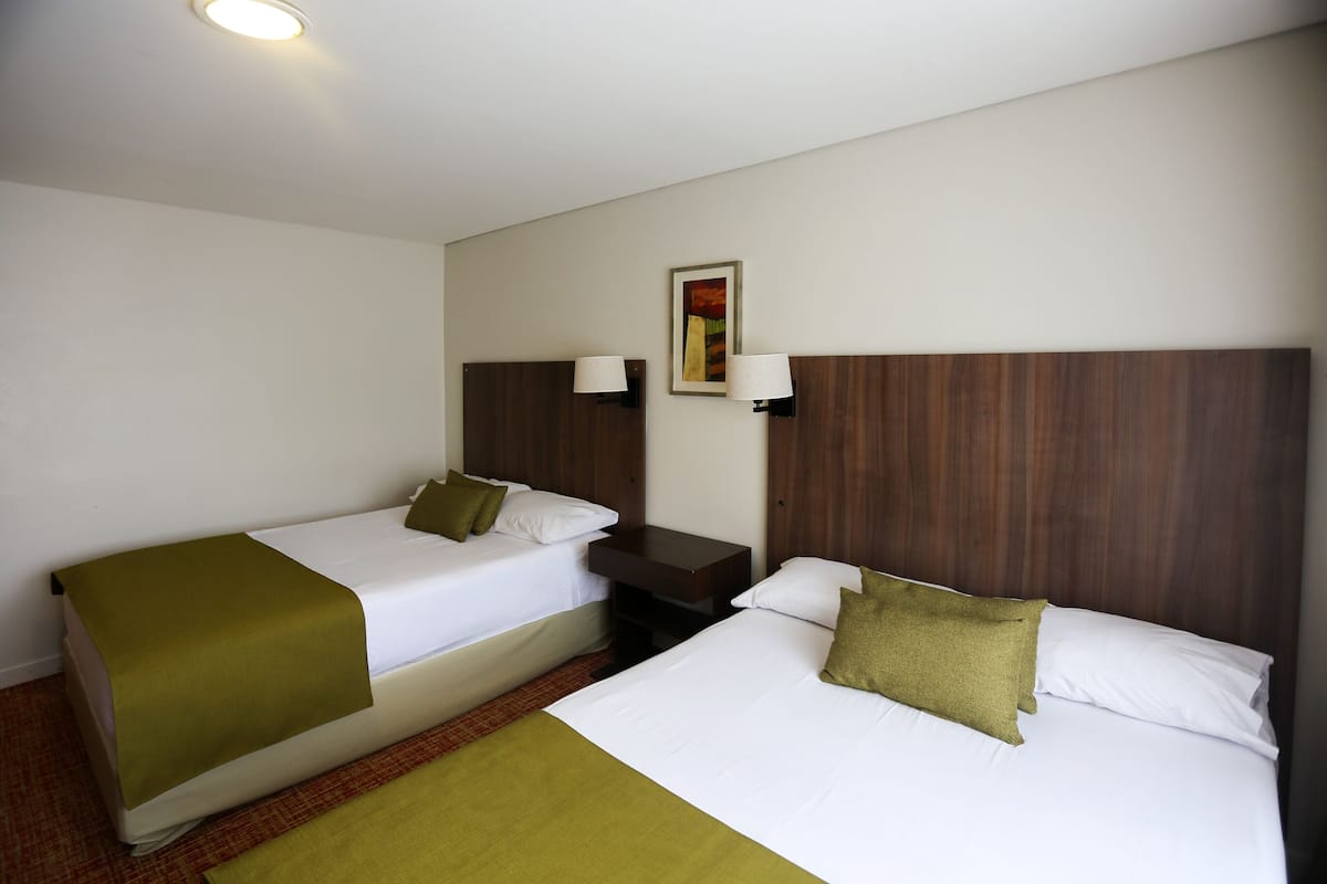 A hotel room with two single beds, a nightstand, a lamp, and a painting on the wall.