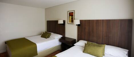 A hotel room with two single beds, a nightstand, a lamp, and a painting on the wall.