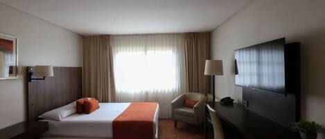 Una habitación de hotel con dos camas, un escritorio, una silla, un televisor y una ventana con cortinas.