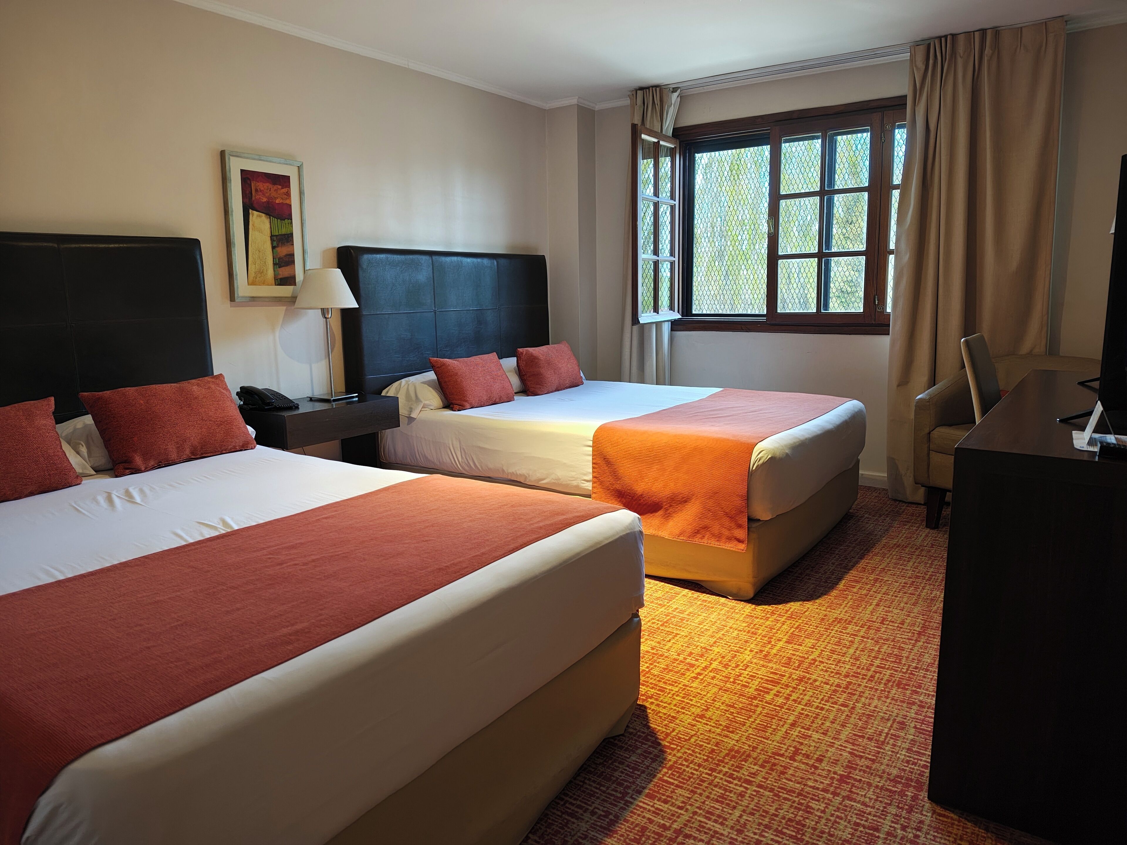 A hotel room with two beds, a desk, a chair, a lamp, and a window with curtains.
