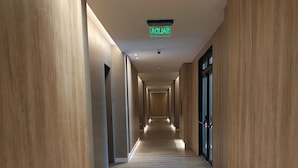 A long, narrow hallway with wooden paneling on the walls and a wooden floor. A green exit sign is visible on the ceiling.