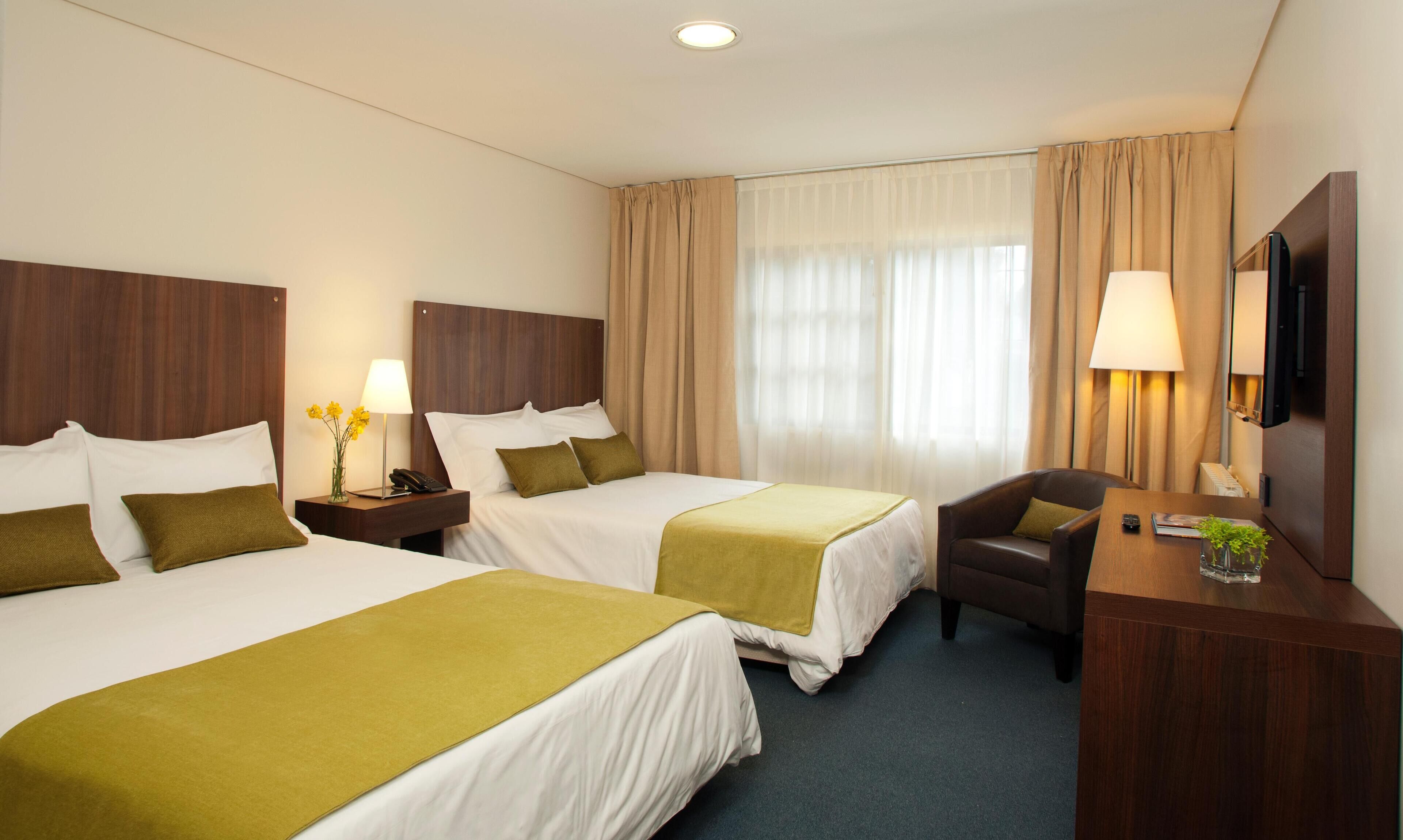 A hotel room with two beds, a desk, a chair, a lamp, and a TV.
