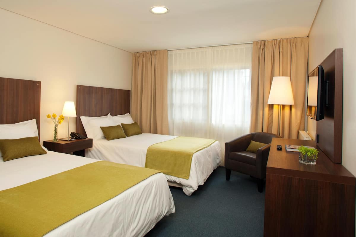 A hotel room with two beds, a desk, a chair, a lamp, and a TV.
