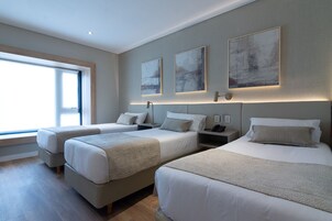 Una habitación de hotel con dos camas individuales, un ventanal grande y tres cuadros abstractos en la pared.