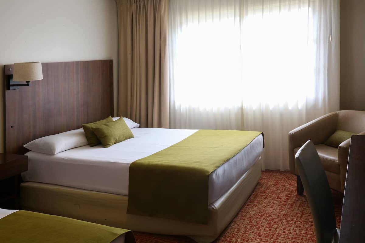 A hotel room with a bed, a chair, a lamp, and a window with curtains.