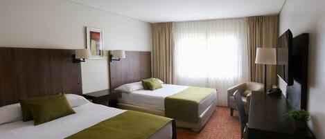 Une chambre d’hôtel avec deux lits, un bureau, une chaise, une télévision et une fenêtre avec des rideaux.