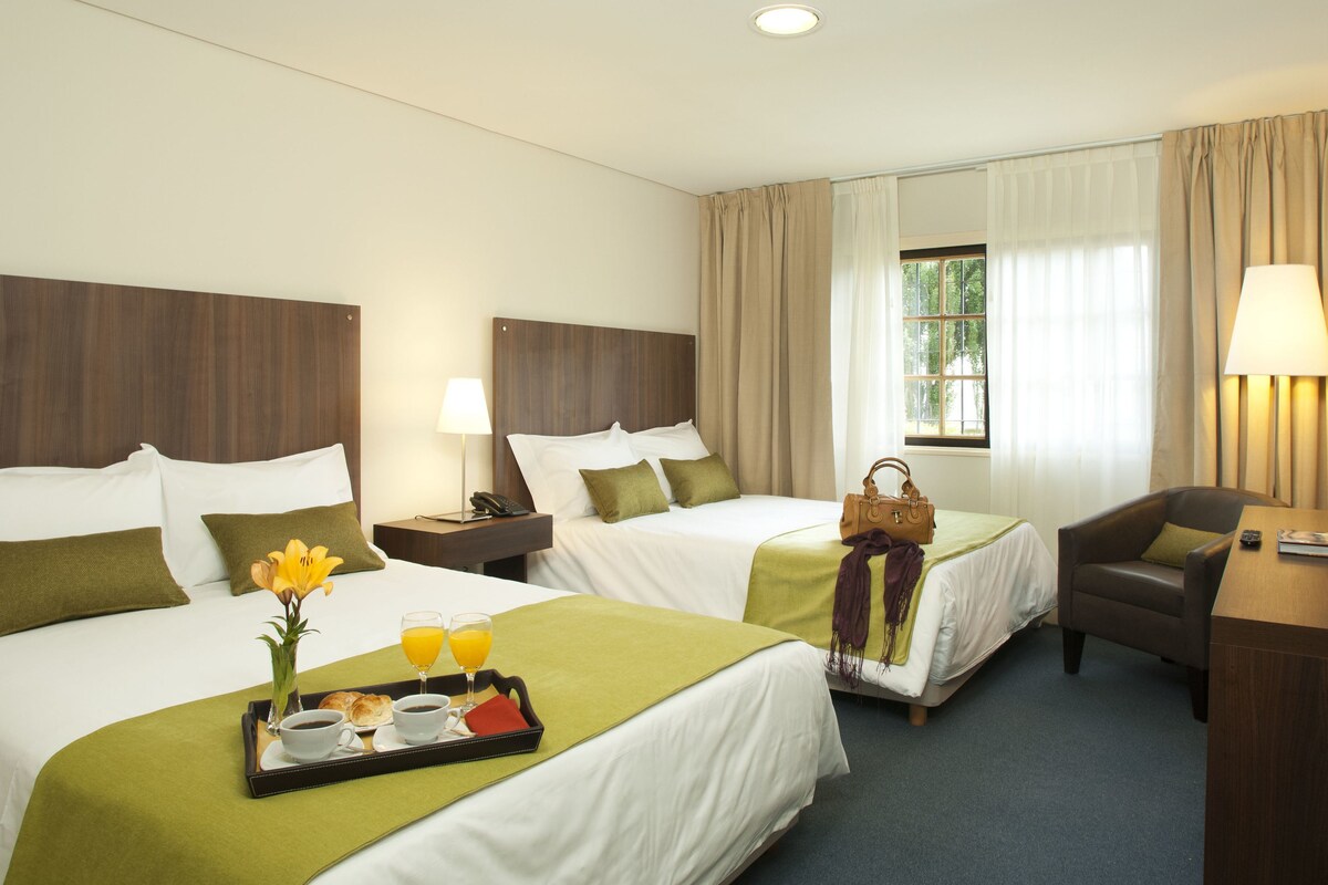 Habitación de hotel con dos camas, un escritorio, una silla, un televisor y una ventana con cortinas.