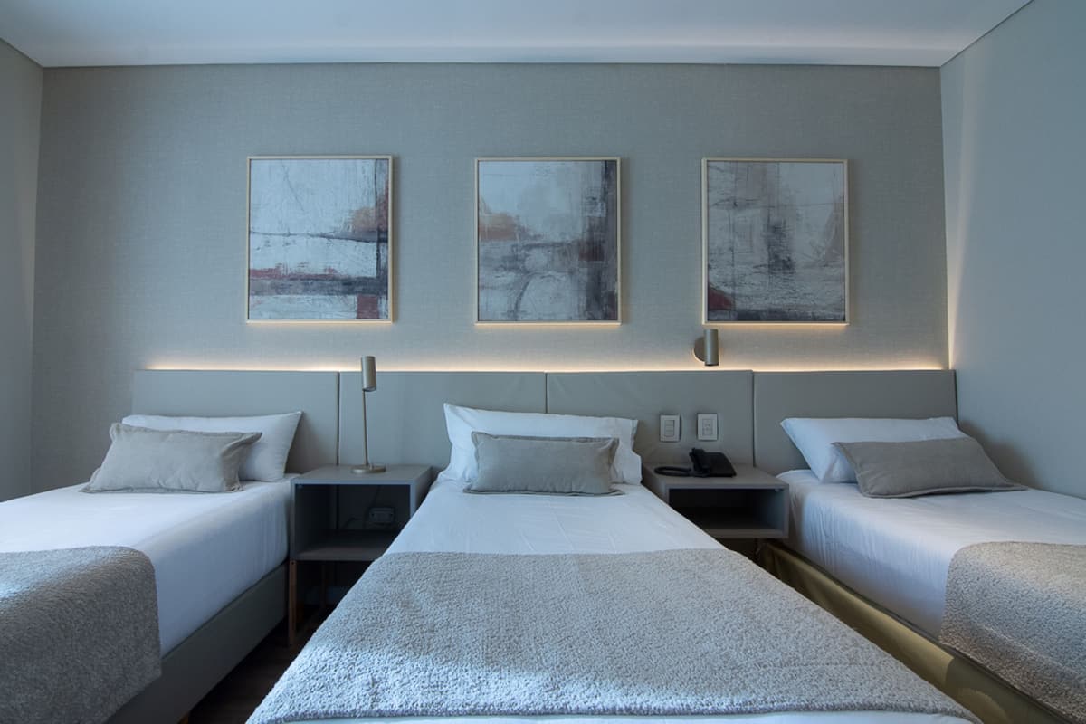 A hotel room with two beds, bedside tables, and three abstract paintings on the wall.