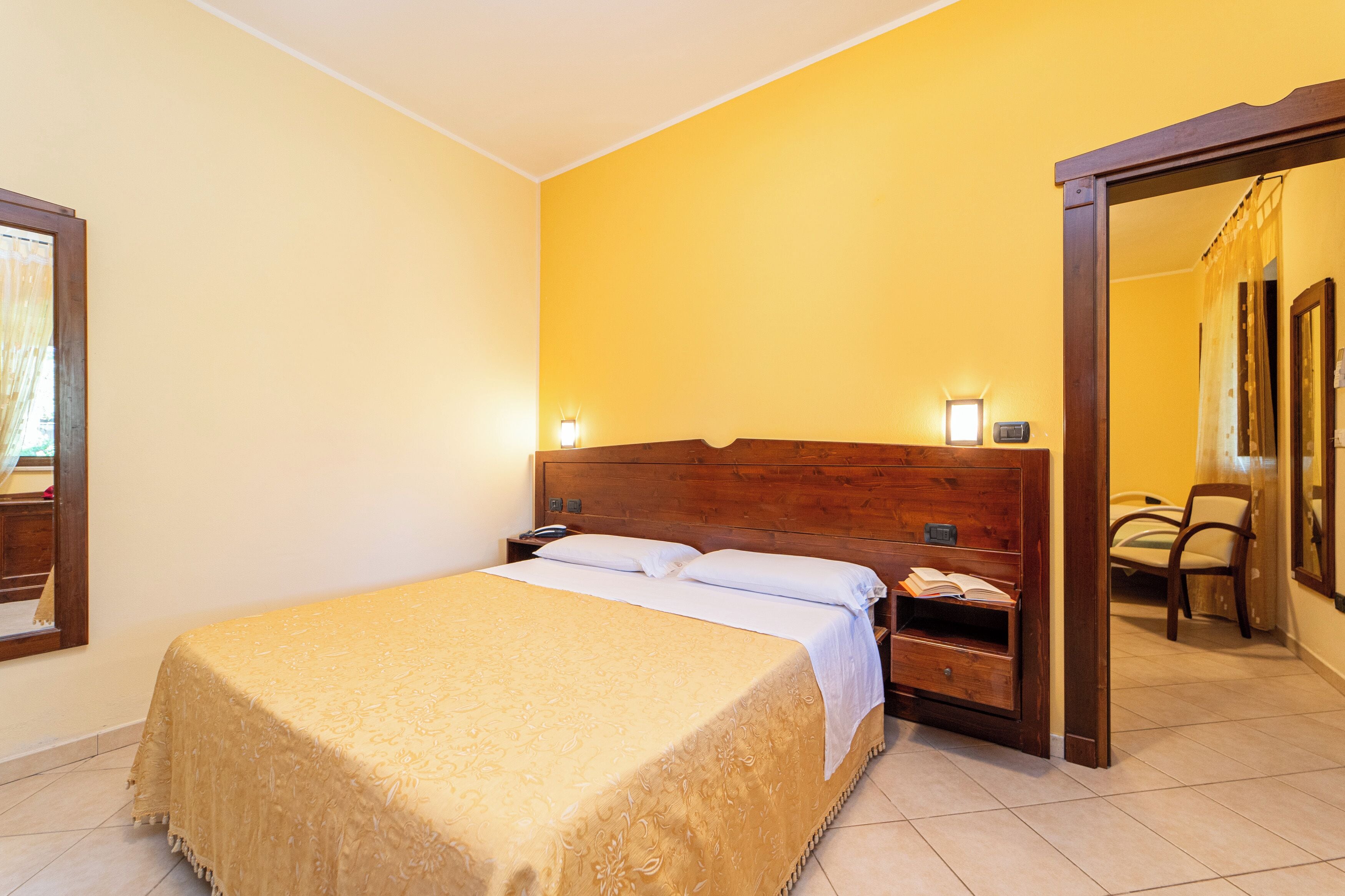 Ein Hotelzimmer mit einem großen Bett, Nachttischlampen, einem Nachttisch und einem Holzkopfteil.