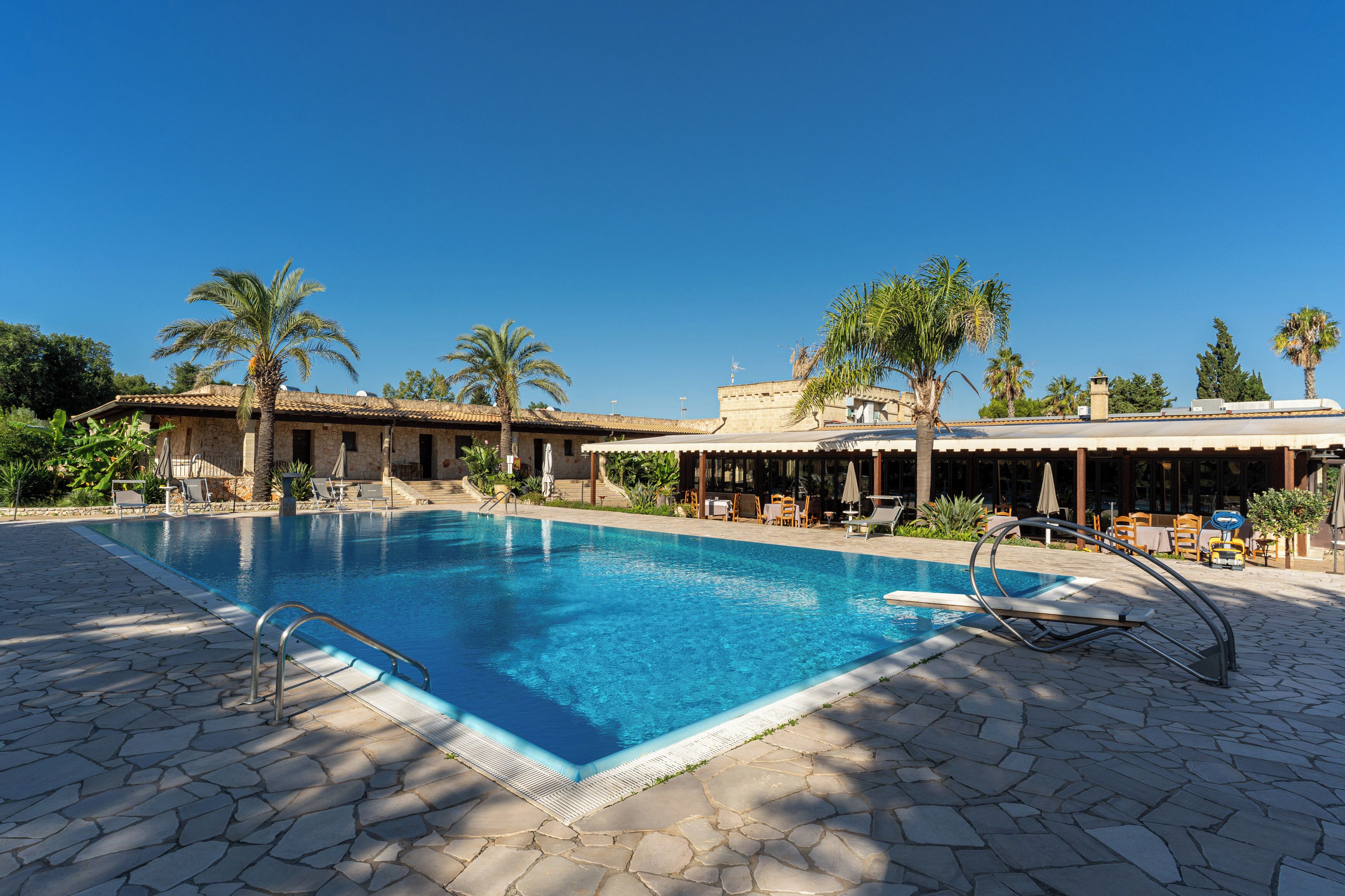 A swimming pool with a stone deck, palm trees, and outdoor seating areas.