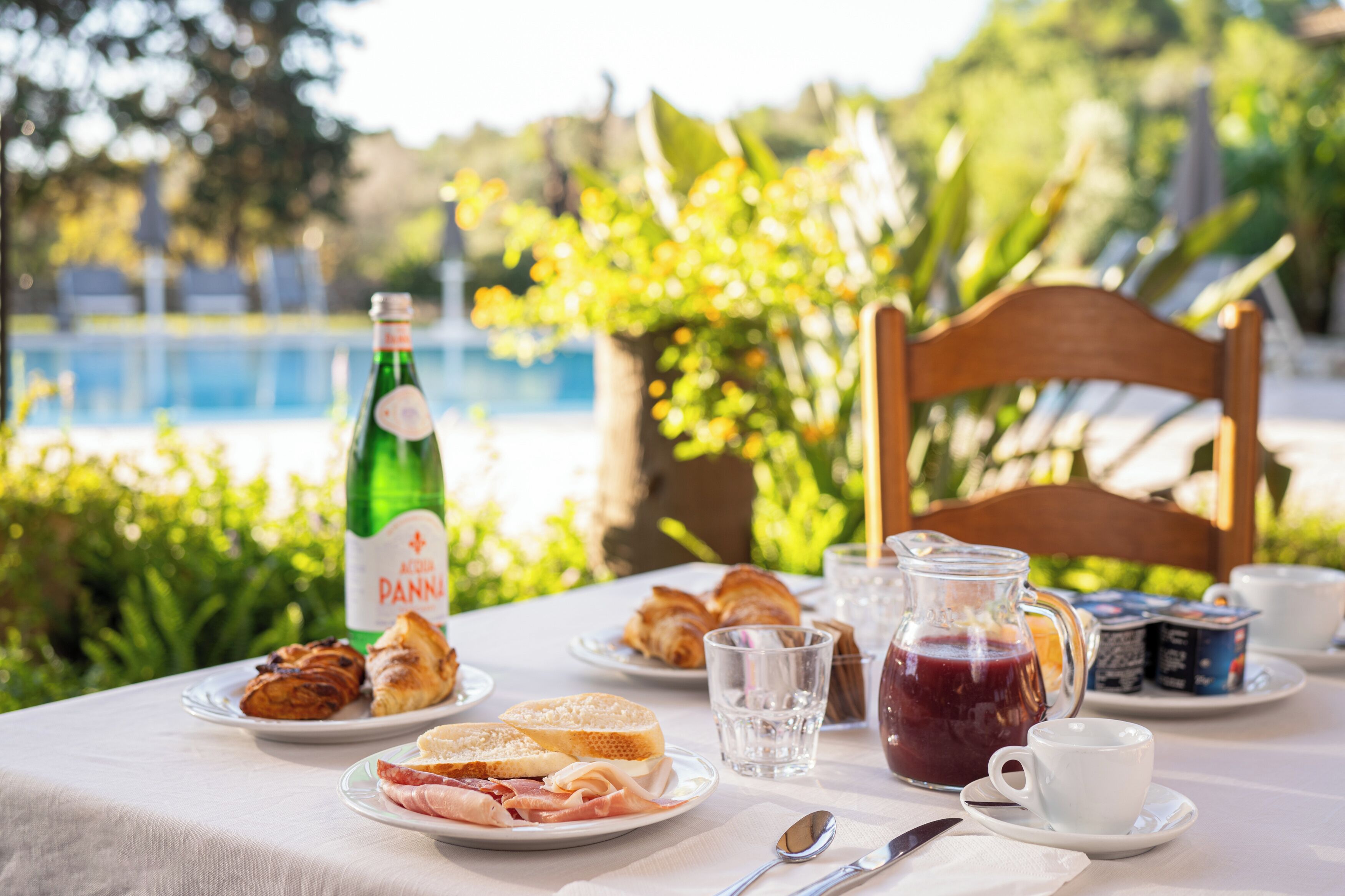 A table set for breakfast with croissants, ham, and bread, a bottle of Acqua Panna, a pitcher of juice, and a cup of coffee.