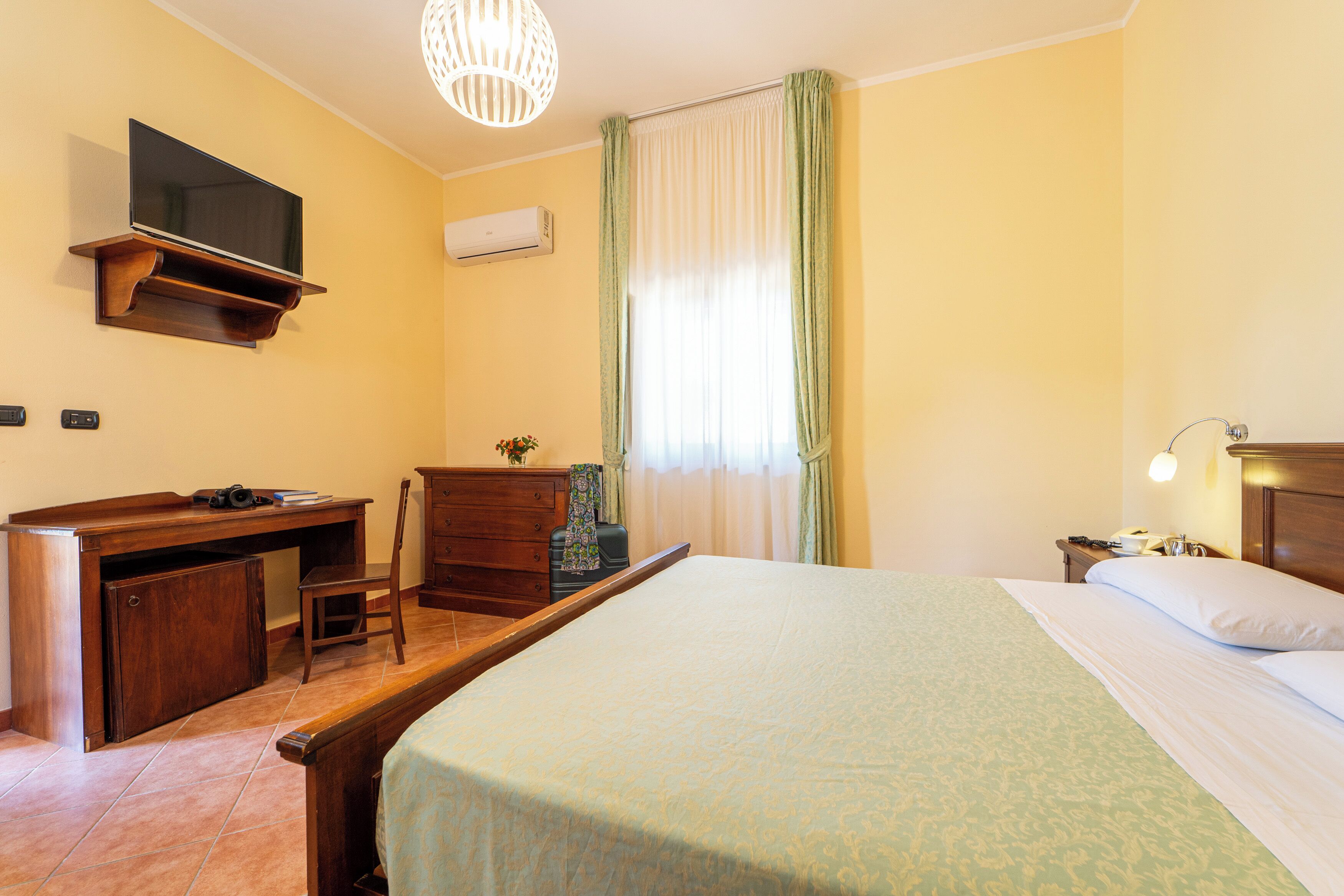 Une chambre d’hôtel équipée d’un lit, d’un bureau, d’une chaise et d’un téléviseur fixé au mur.