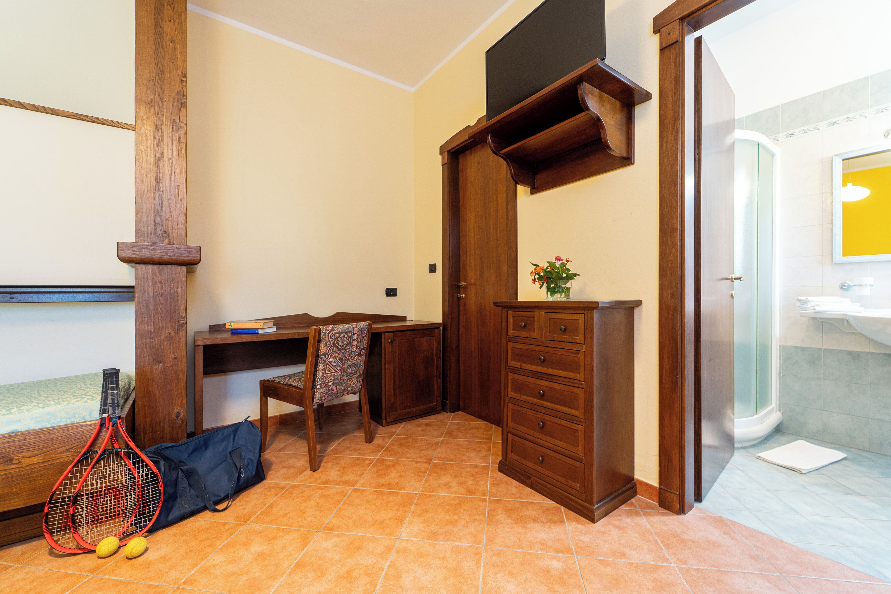 Une pièce avec un bureau en bois, une chaise et un petit meuble. On peut voir une raquette de tennis et des balles sur le sol.