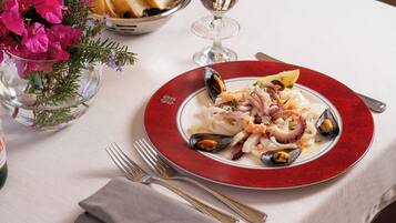 A seafood dish on a red plate with a glass of water and bread on the table.