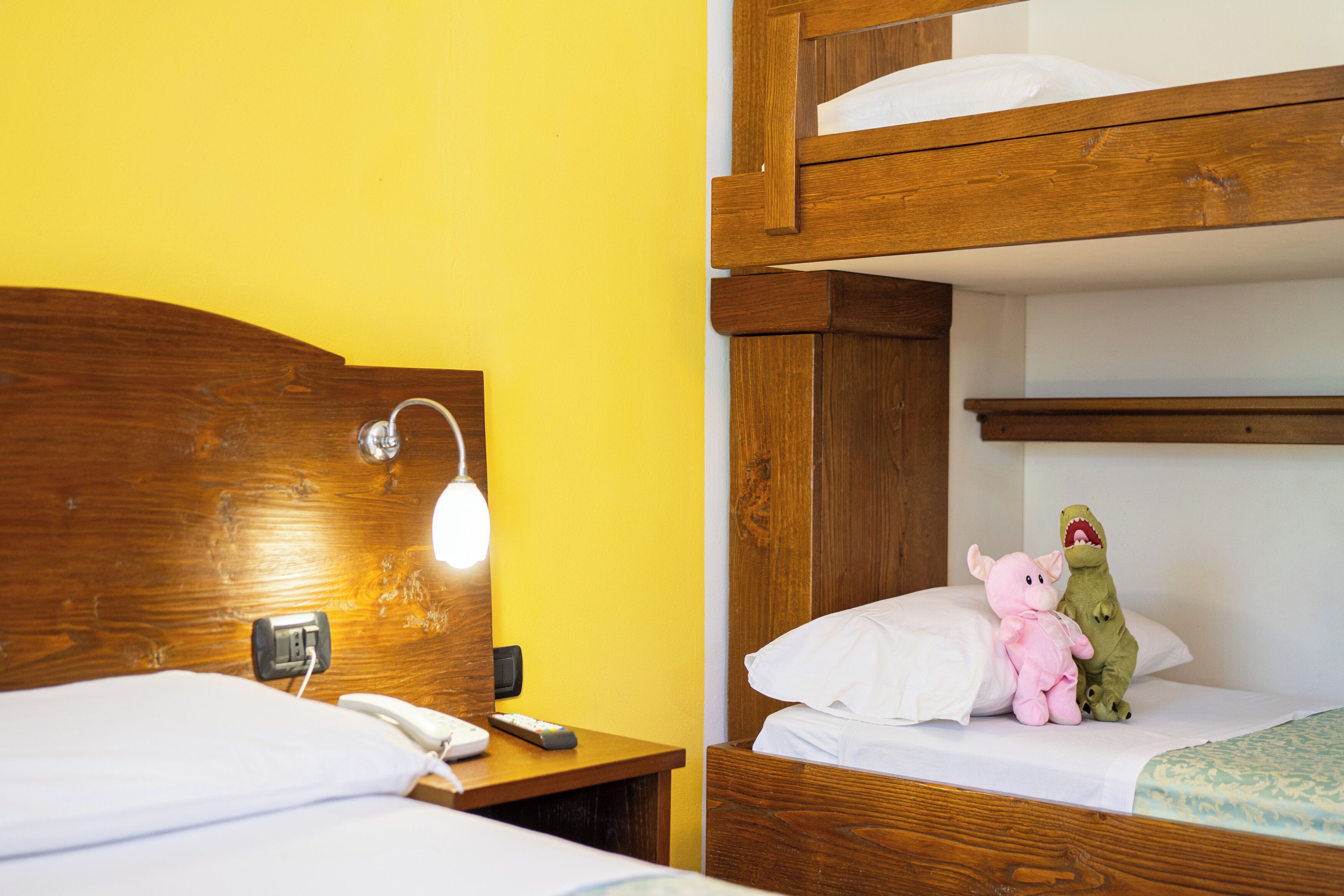 A hotel room with a wooden bunk bed, a bedside table with a lamp, and a telephone.