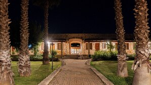 A paved pathway leading to a building with a stone facade and arched entrance, surrounded by palm trees and well-lit by street lamps. - Hotel Masseria Le Pajare (Presicce-Acquarica)