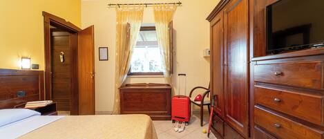 Una habitación de hotel con cama, armario, televisor y ventana con cortinas.