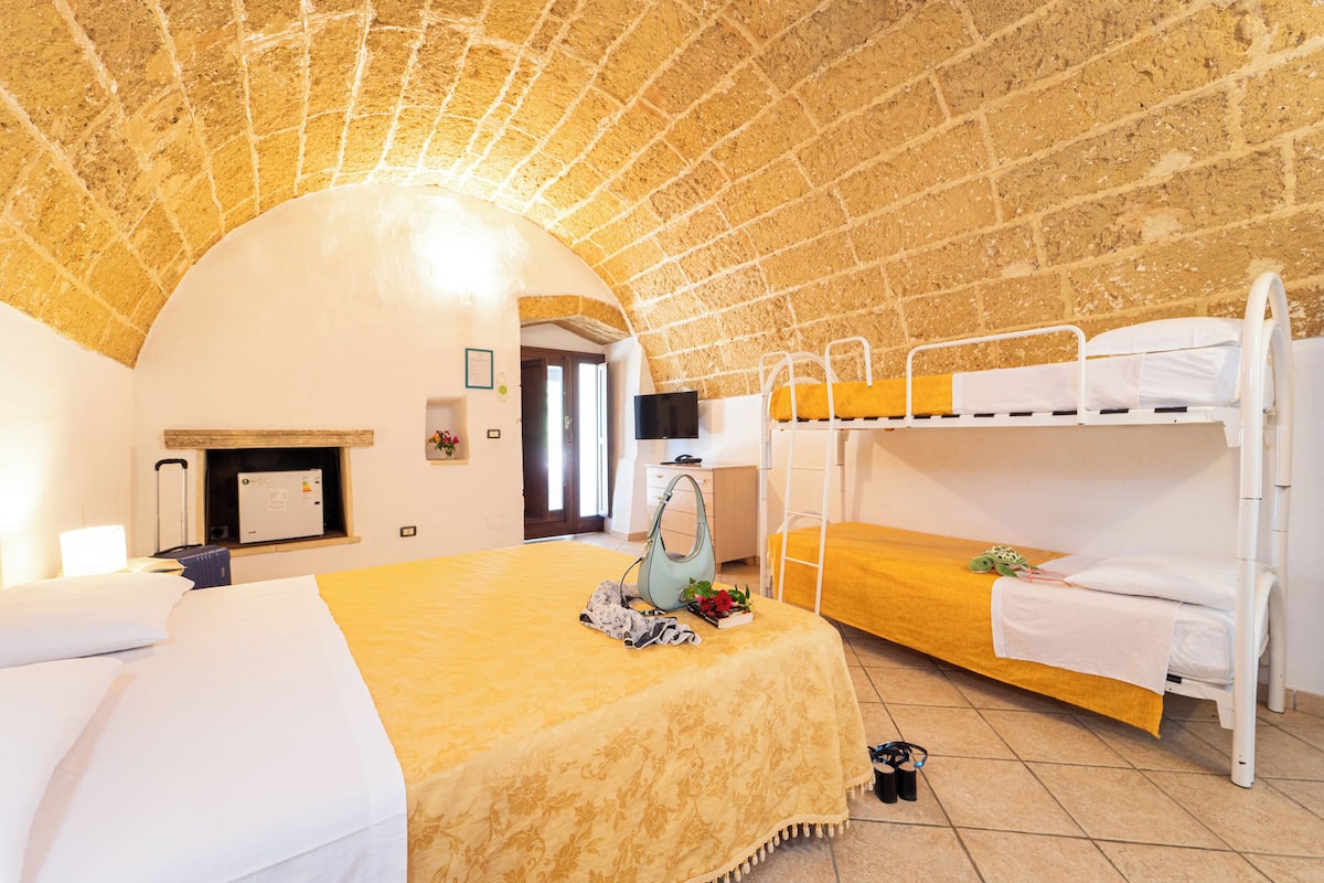 A room with a brick ceiling, a bunk bed, a single bed, a desk, and a TV.