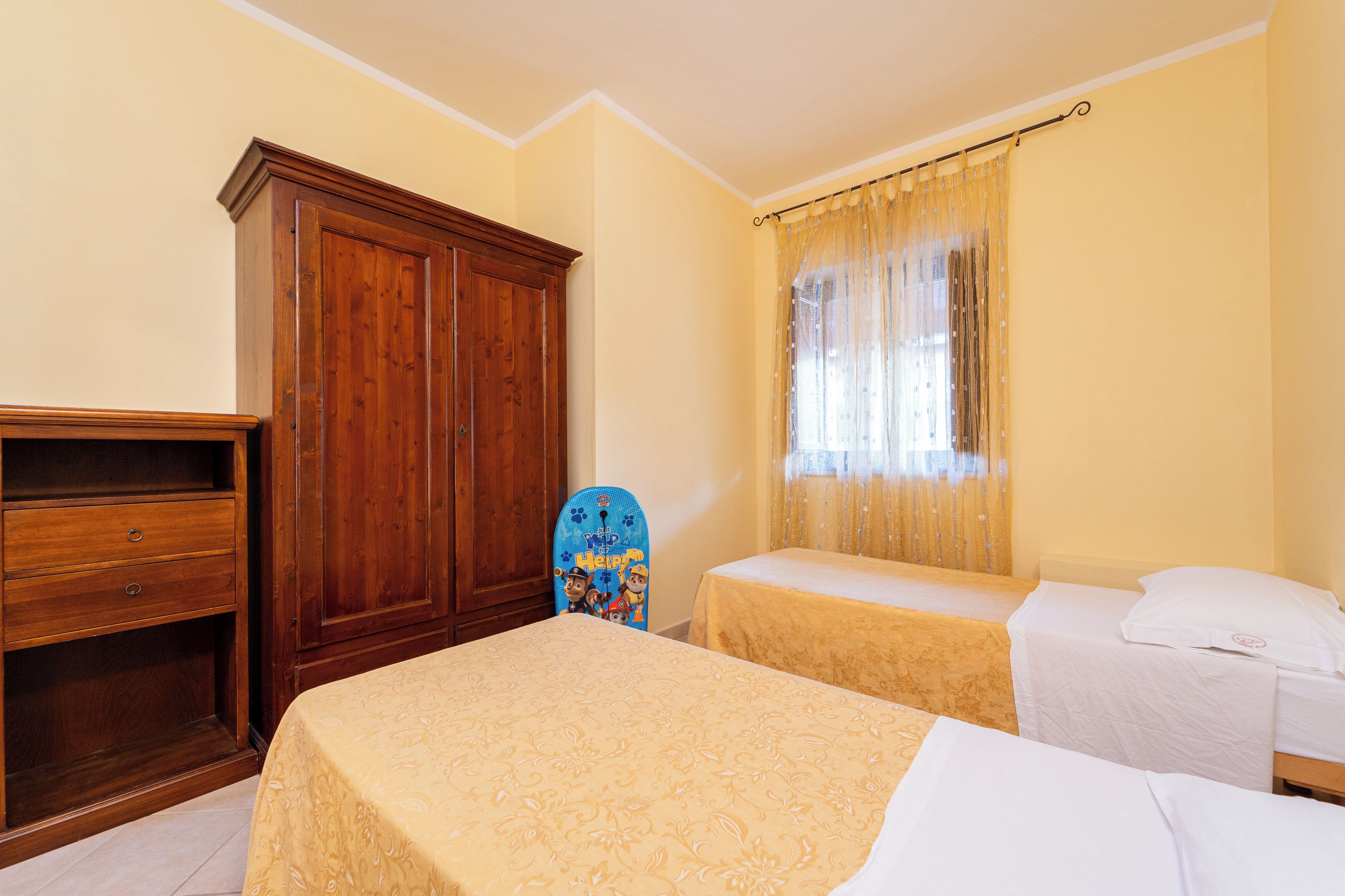 A bedroom with two beds, a wardrobe, and a window with curtains.