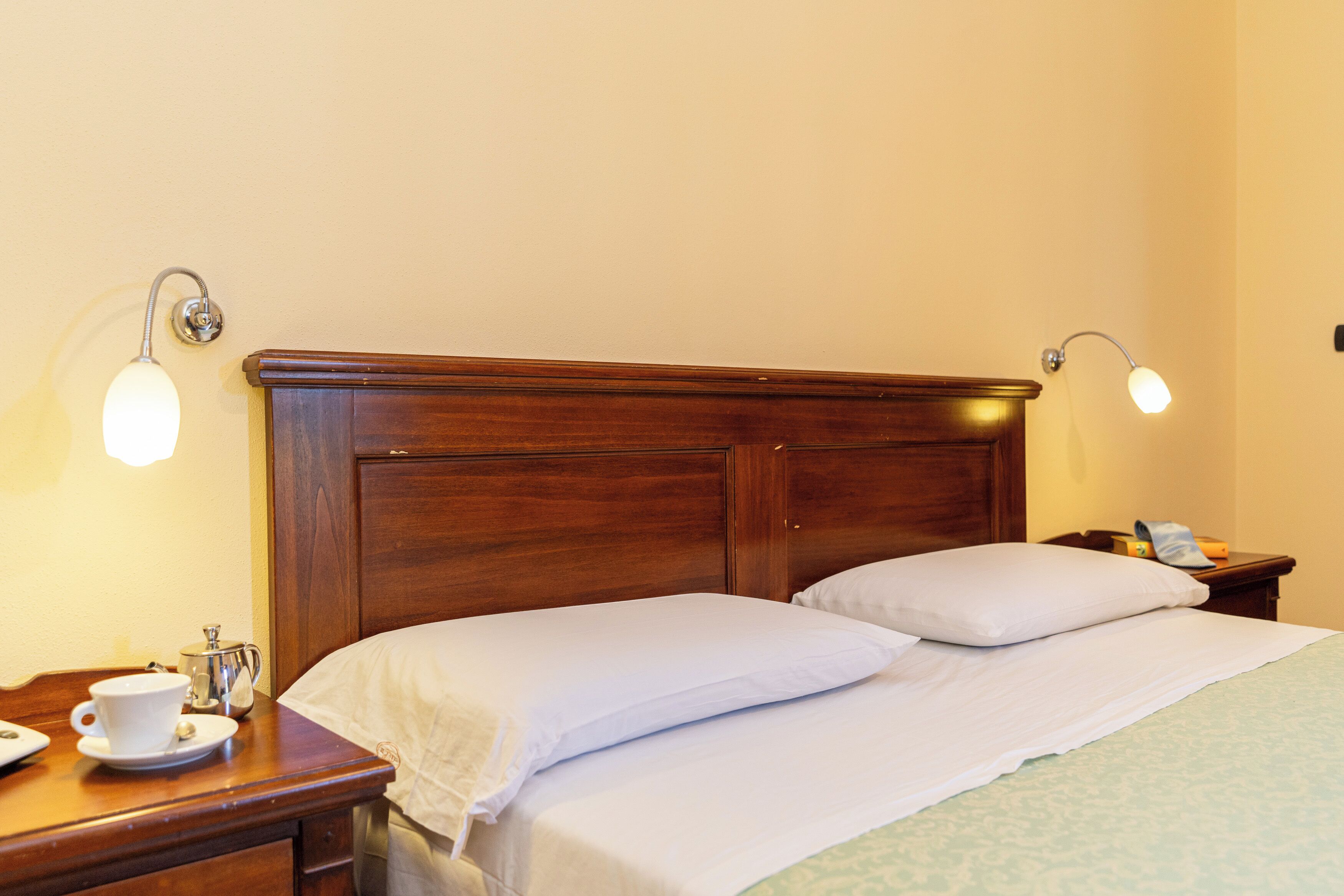 Un letto rifatto con lenzuola bianche, una testiera in legno e due abat-jour.