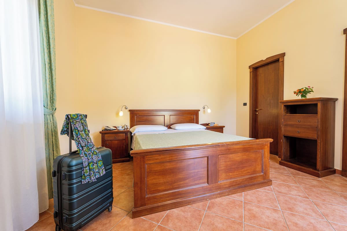 A bedroom with a wooden bed, a nightstand, a dresser, and a suitcase.