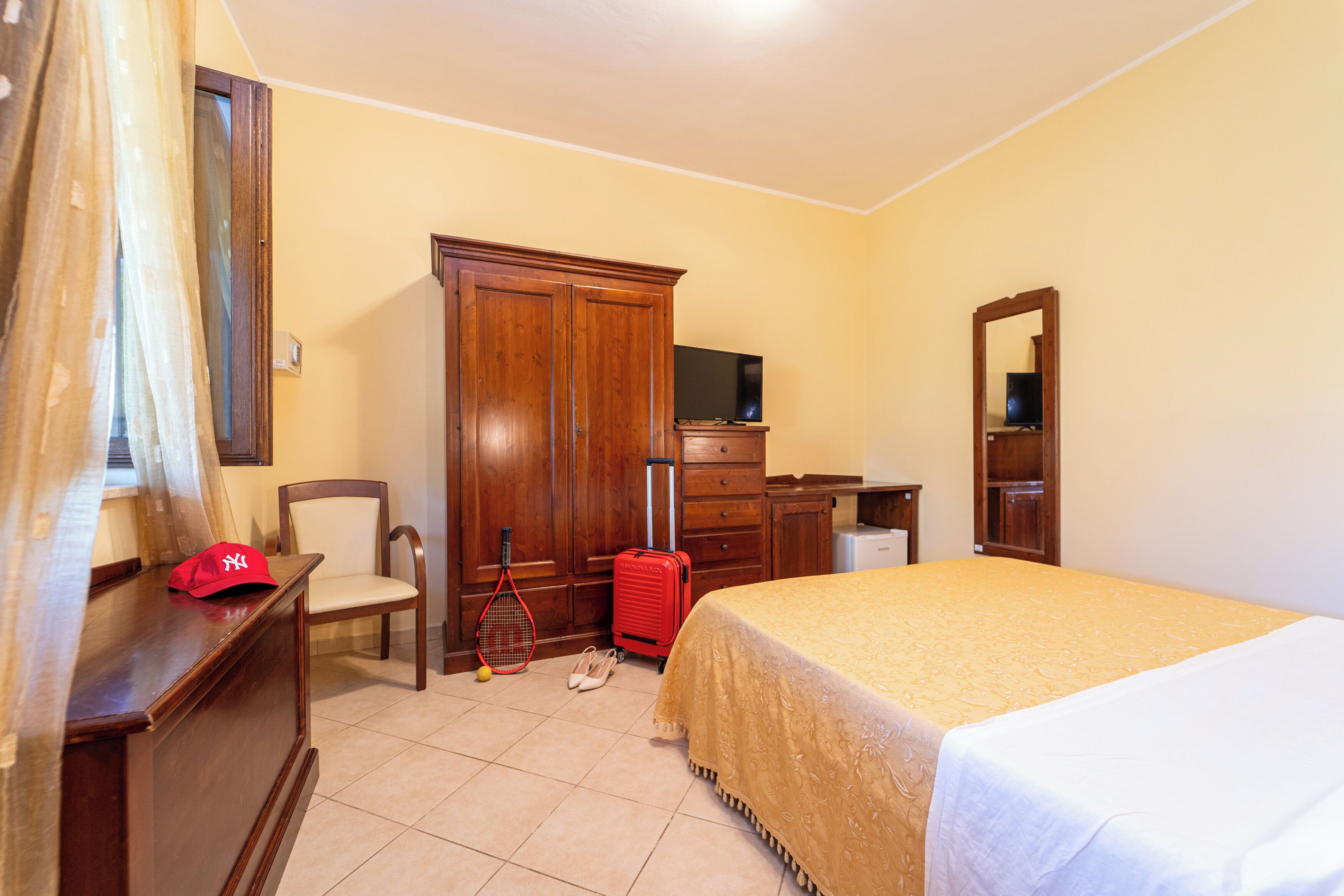 A hotel room with a bed, a desk, a chair, a wardrobe, a television, and a mirror.
