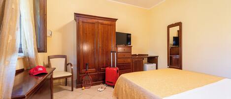 A hotel room with a bed, a desk, a chair, a wardrobe, a television, and a mirror.