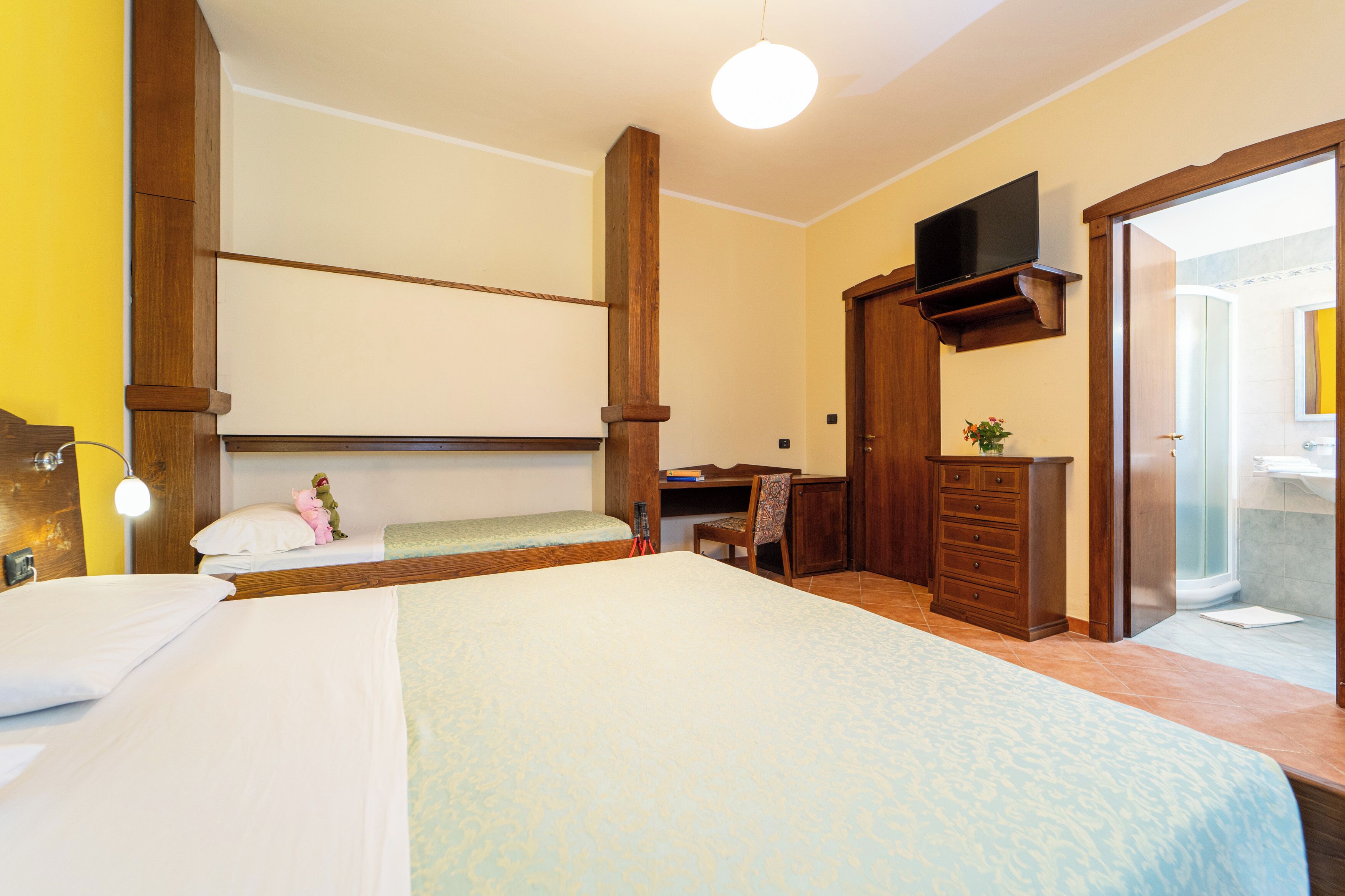 Une chambre d’hôtel avec un grand lit, un bureau, une chaise, une télévision et une salle de bain visible à travers une porte ouverte.