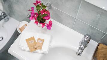 Ein Waschbecken mit weißem Handtuch, zwei Haarpflegeprodukten und einem Blumentopf mit rosa Blüten.