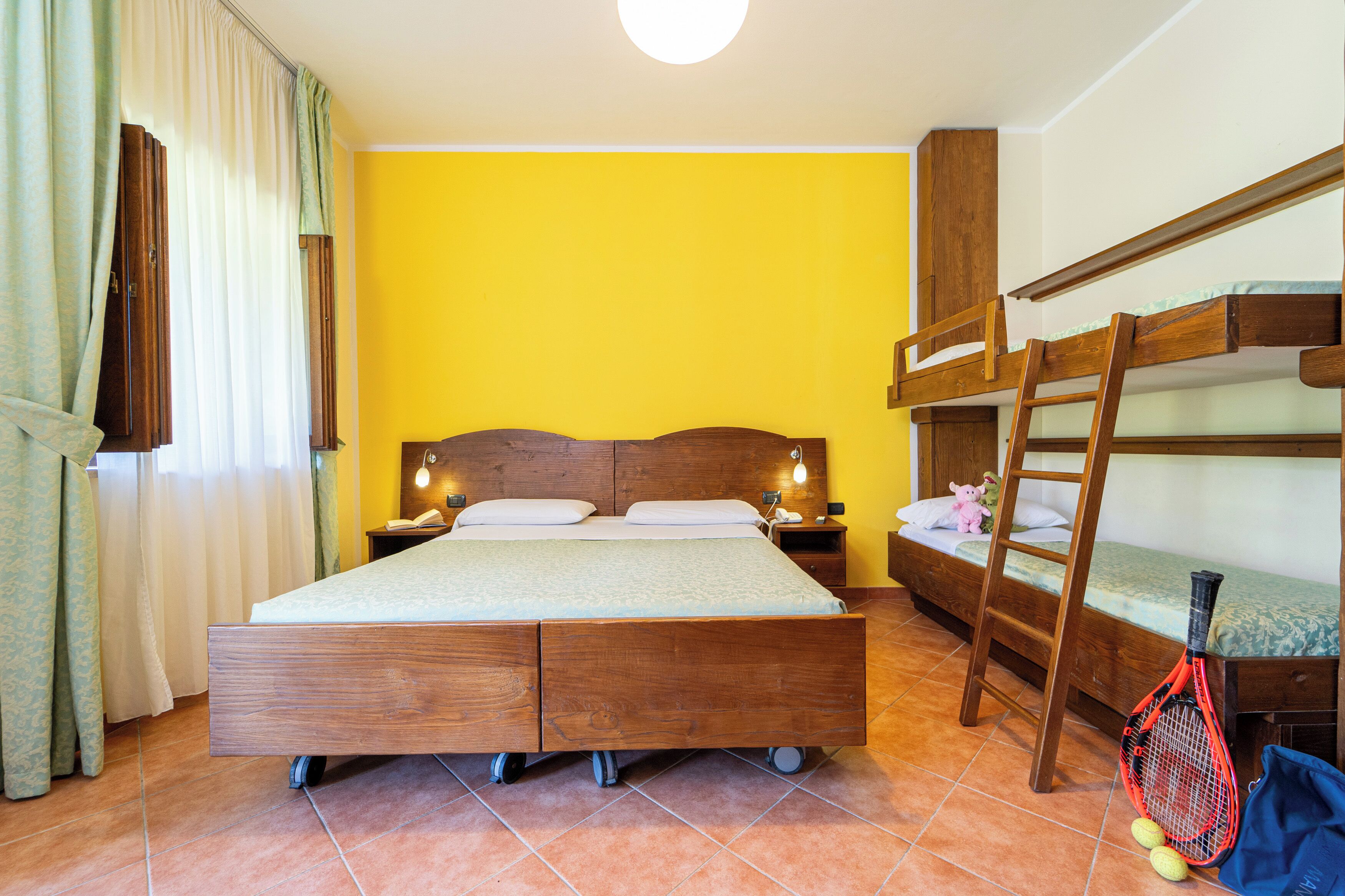 A room with a large bed, bunk beds, a ladder, and a tennis racket.