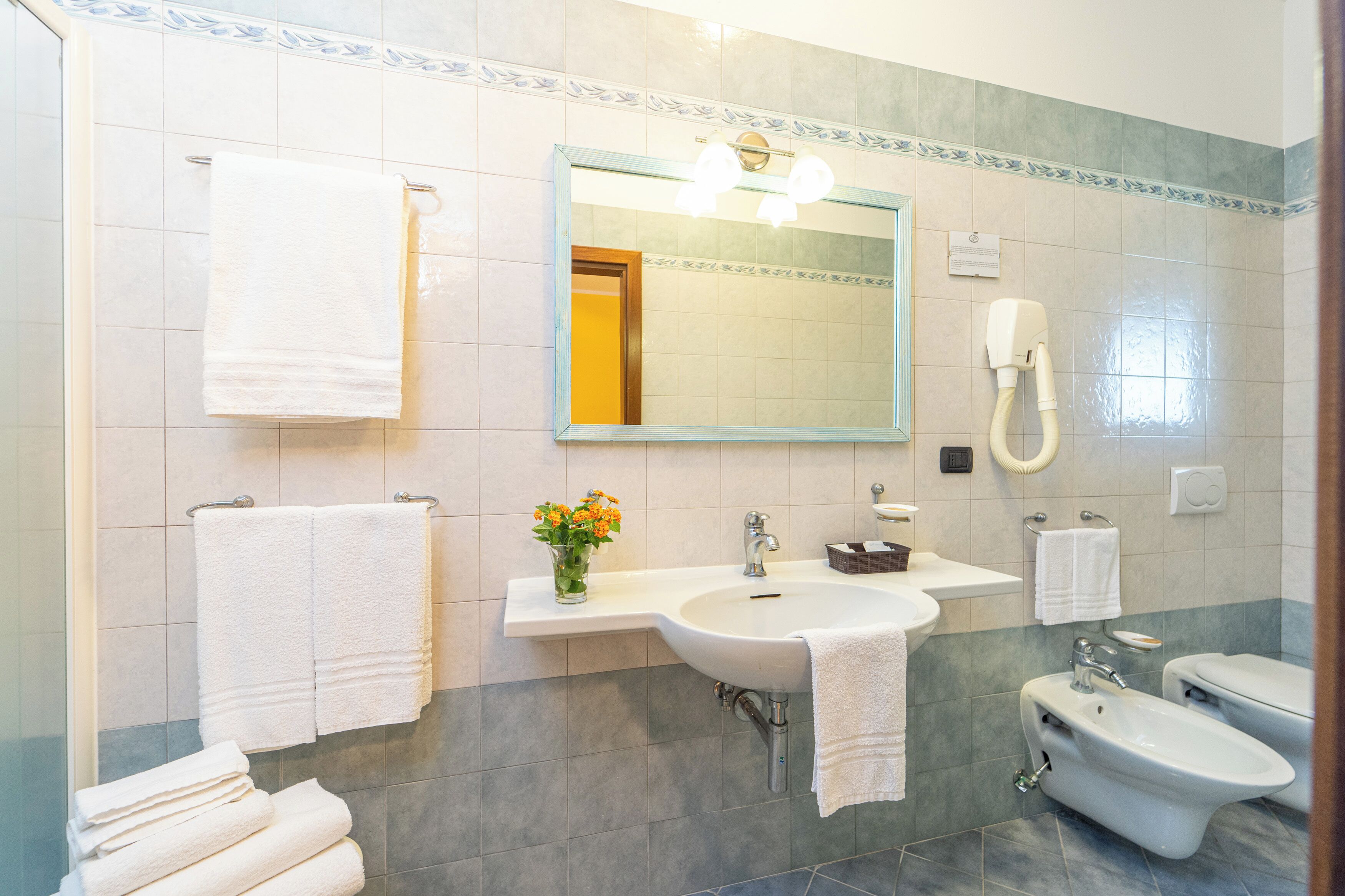 A bathroom with a sink, mirror, towel rack, bidet, and a vase with flowers.