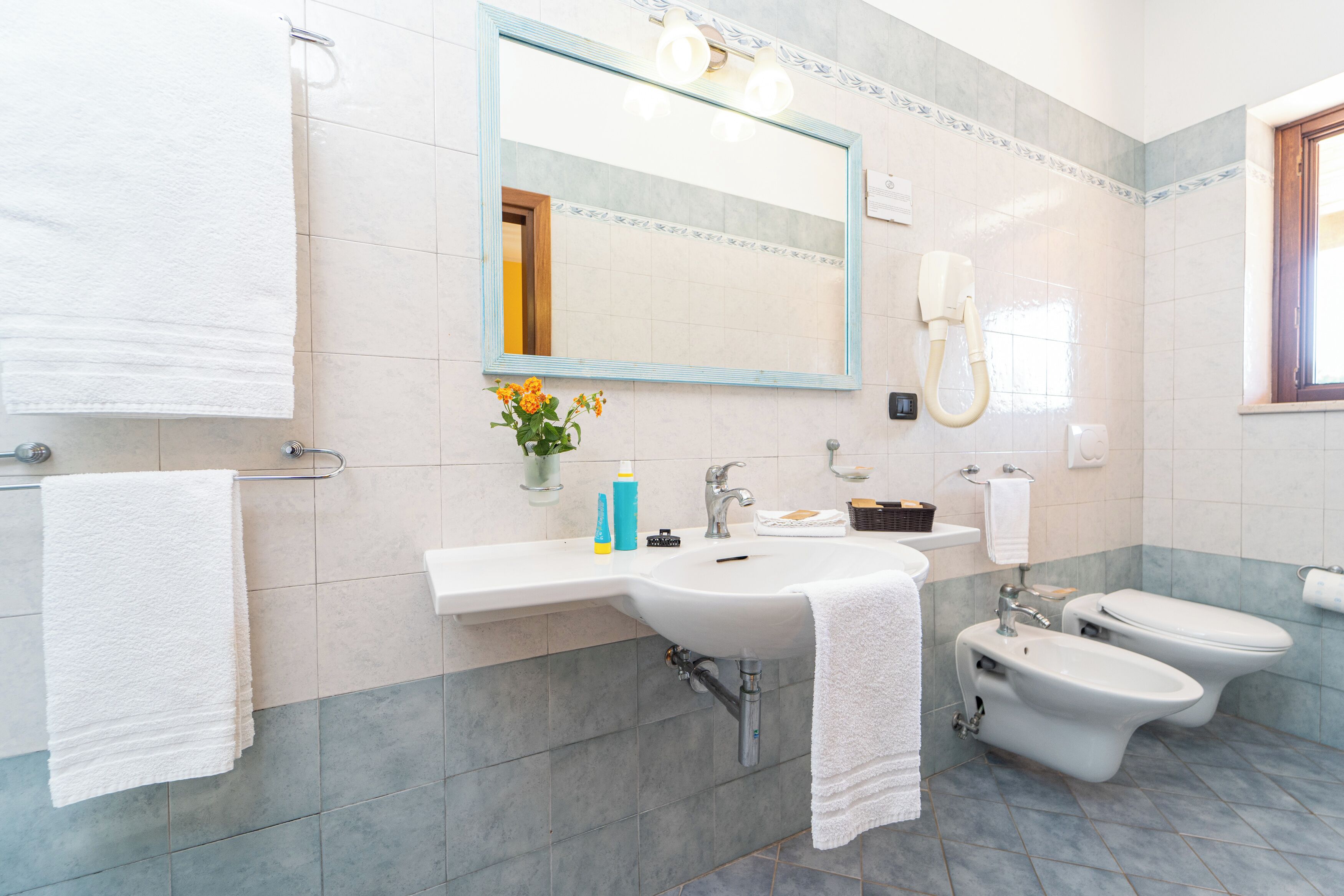 A modern bathroom with a sink, mirror, towel rack, bidet, and toilet.