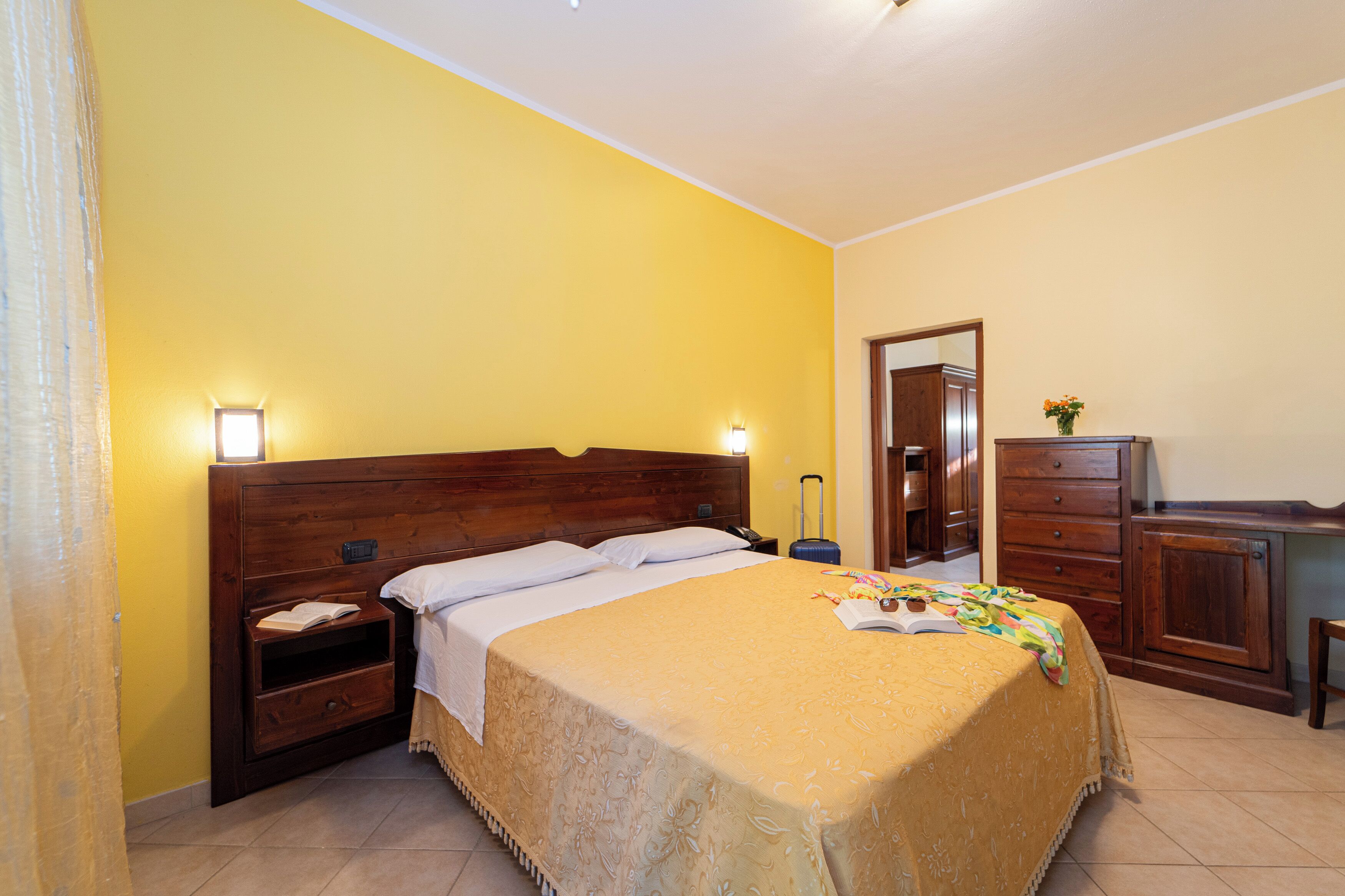A hotel room with a wooden bed, a nightstand, a suitcase, and a dresser.