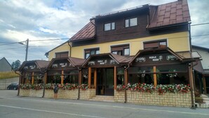 Un edificio de dos plantas con techo marrón y paredes amarillas, con varios comercios que muestran letreros de 'Ozujski Pivo' y 'Bijela Ruza'.