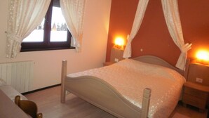 Un dormitorio con cama, dos mesitas de noche, una ventana con cortinas y una lámpara de pared.